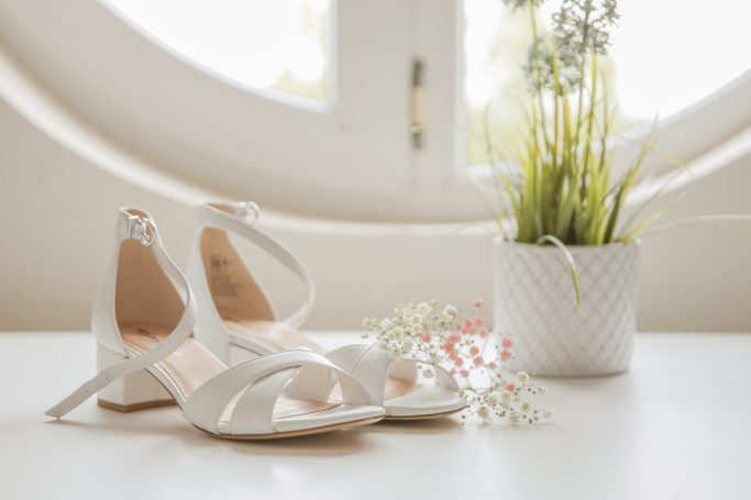 Weiße Halbschuhe neben einer weißen Blumentöpfen mit Pflanzen und kleinen Blumen.