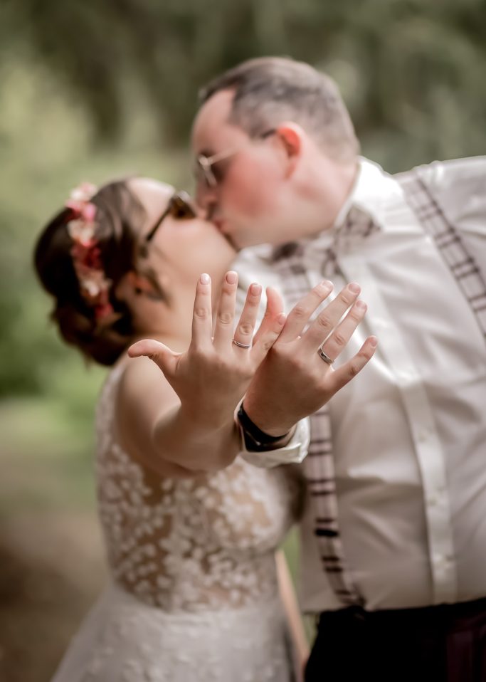 Braut und Bräutigam küssen sich, Hände hochgehoben, in einem romantischen Außenbereich.