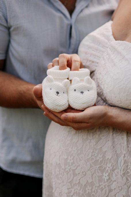 Weiße Babyschuhe mit Tiermotiven, gehalten von einer schwangeren Person.